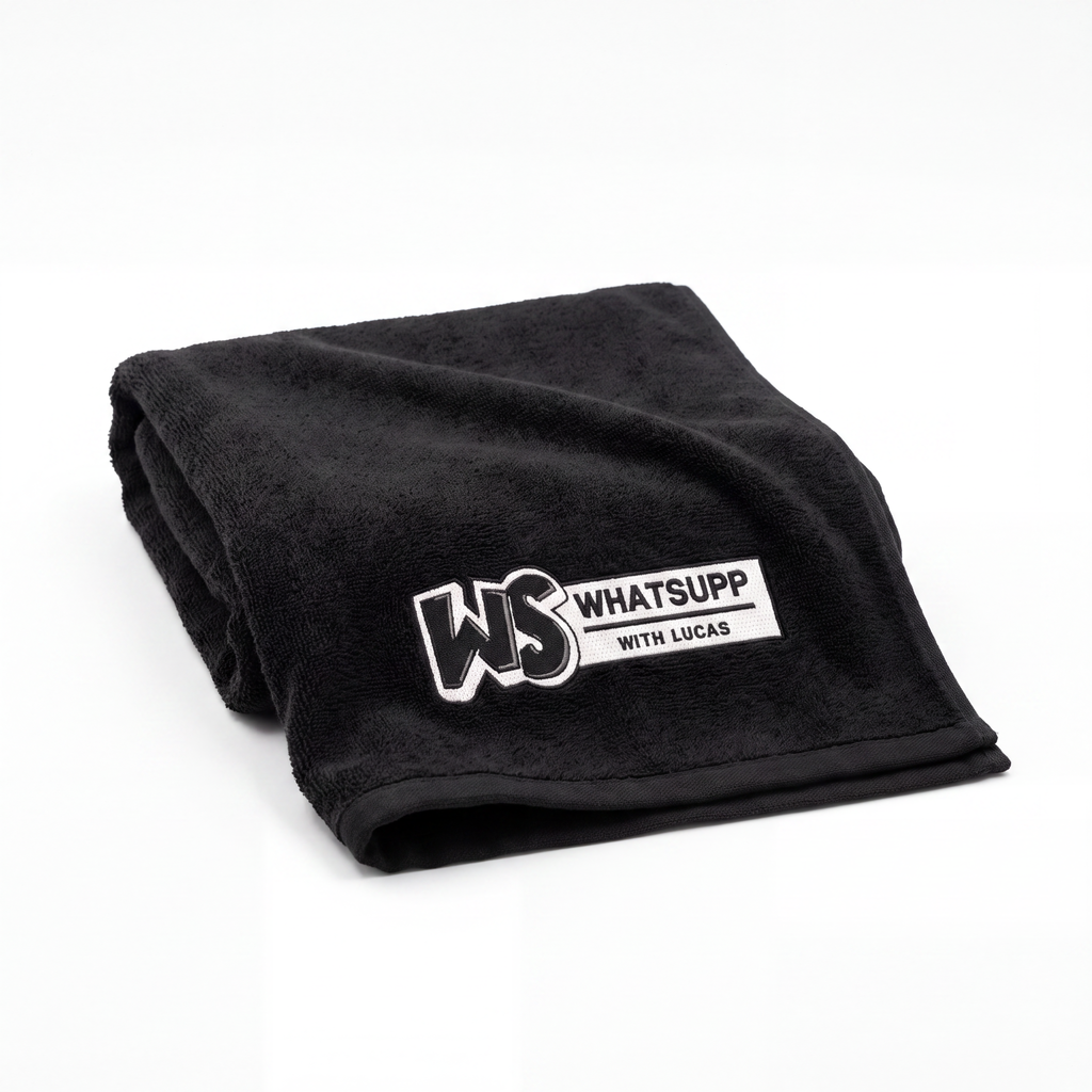 Black Whatsuppwithlucas gym towel folded lengthwise, close-up on the embroidered WS logo patch
