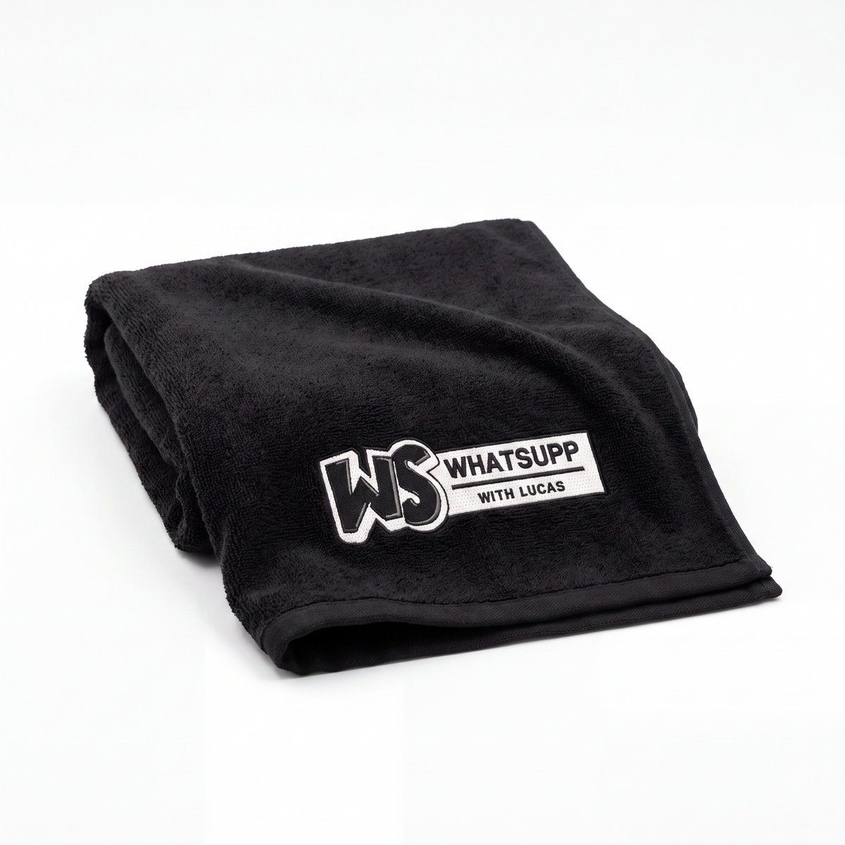 Black Whatsuppwithlucas gym towel folded lengthwise, close-up on the embroidered WS logo patch